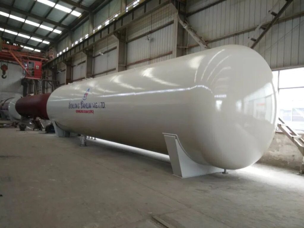 Large white horizontal pressure vessel on saddle supports inside a fabrication hall