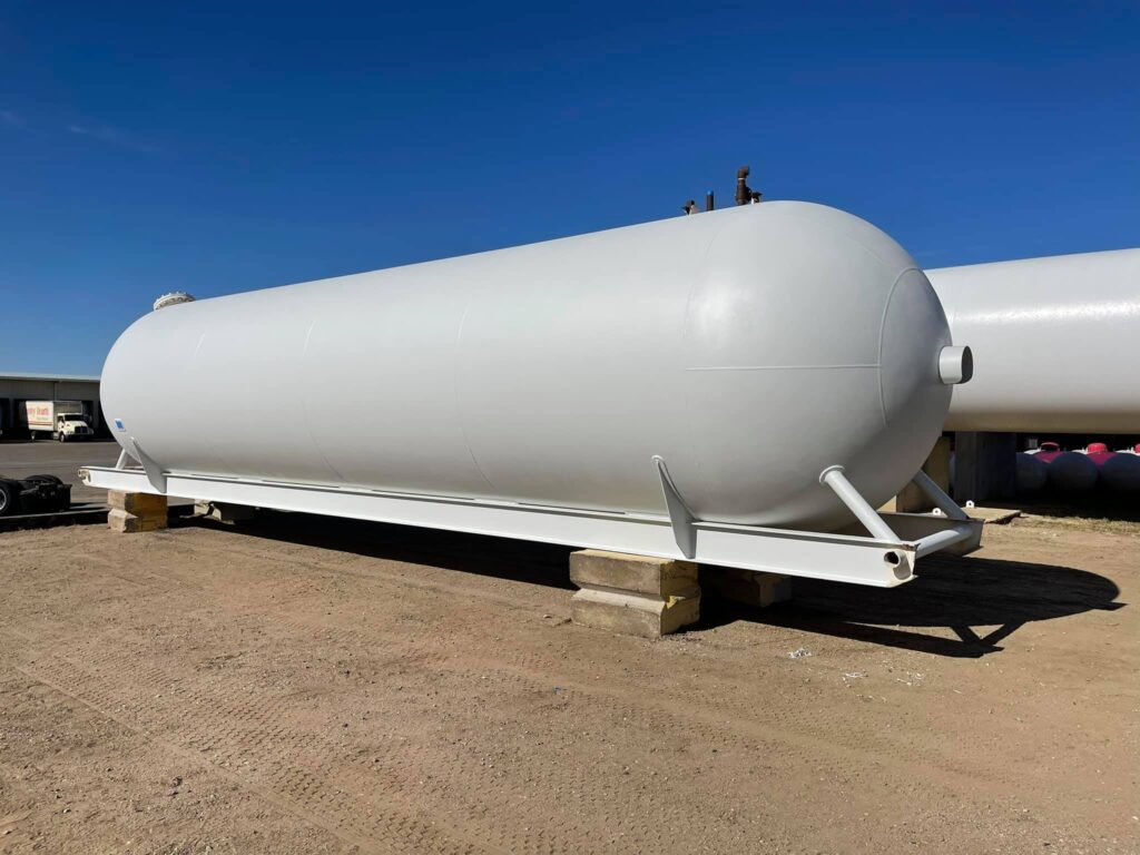 Large white skid-mounted propane storage tank standing on wooden blocks